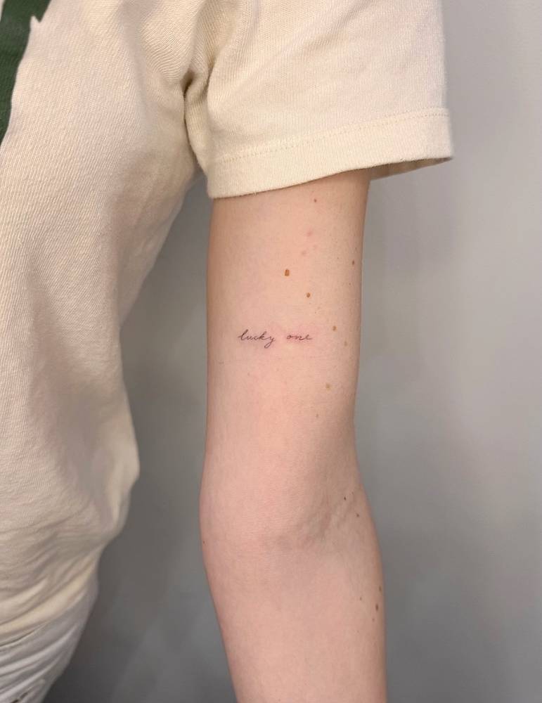 Lettering tattoo that says "lucky me" in handwritten font.