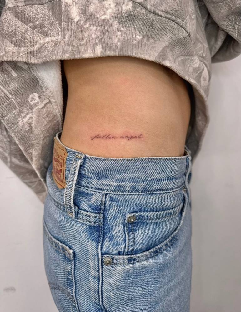 "Fallen angel" lettering tattoo located on the hip.