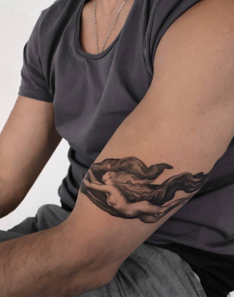 Nude woman tattoo in classical style located on the upper arm.