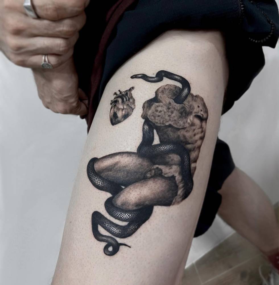 Snake wrapped around a sculpture tattooed on the thigh.