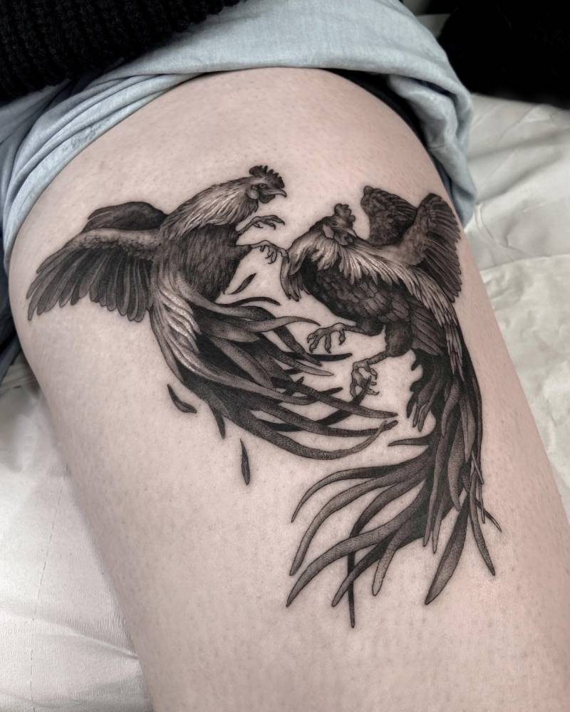 Cockfighting tattoo in black and grey style located on the thigh.
