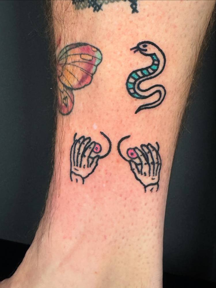 Hands holding breasts and snake in traditional style tattooed on the ankle.