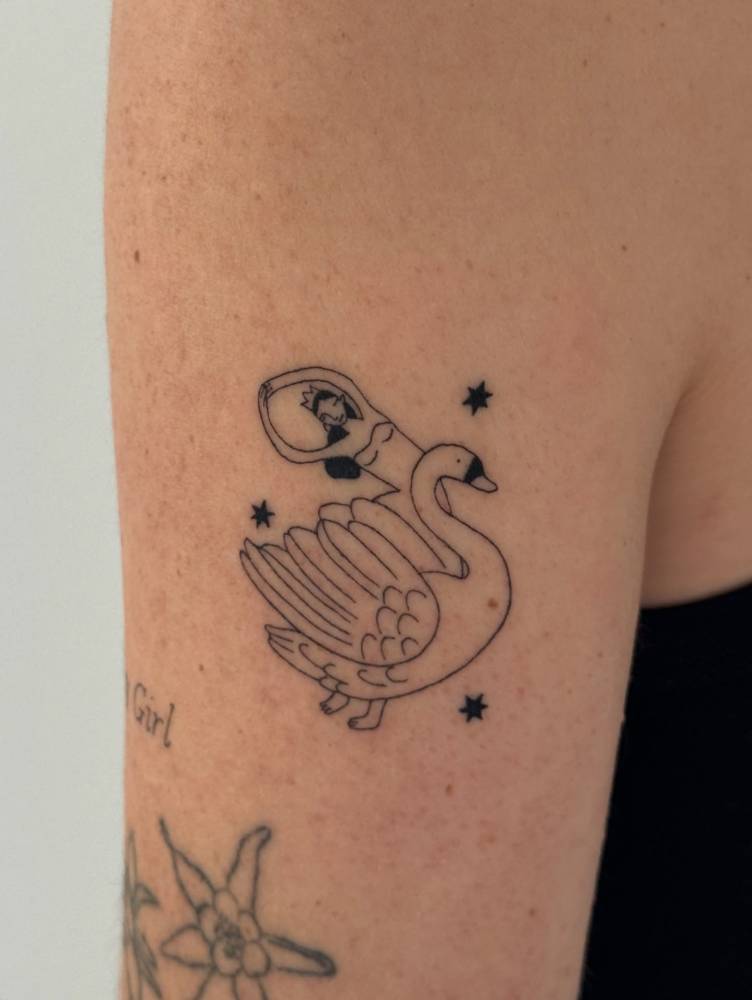 Swan and woman tattoo in illustrative style placed on the upper arm.