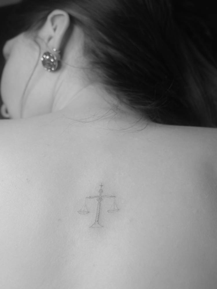 Scale tattoo in fine line style done on the upper back.