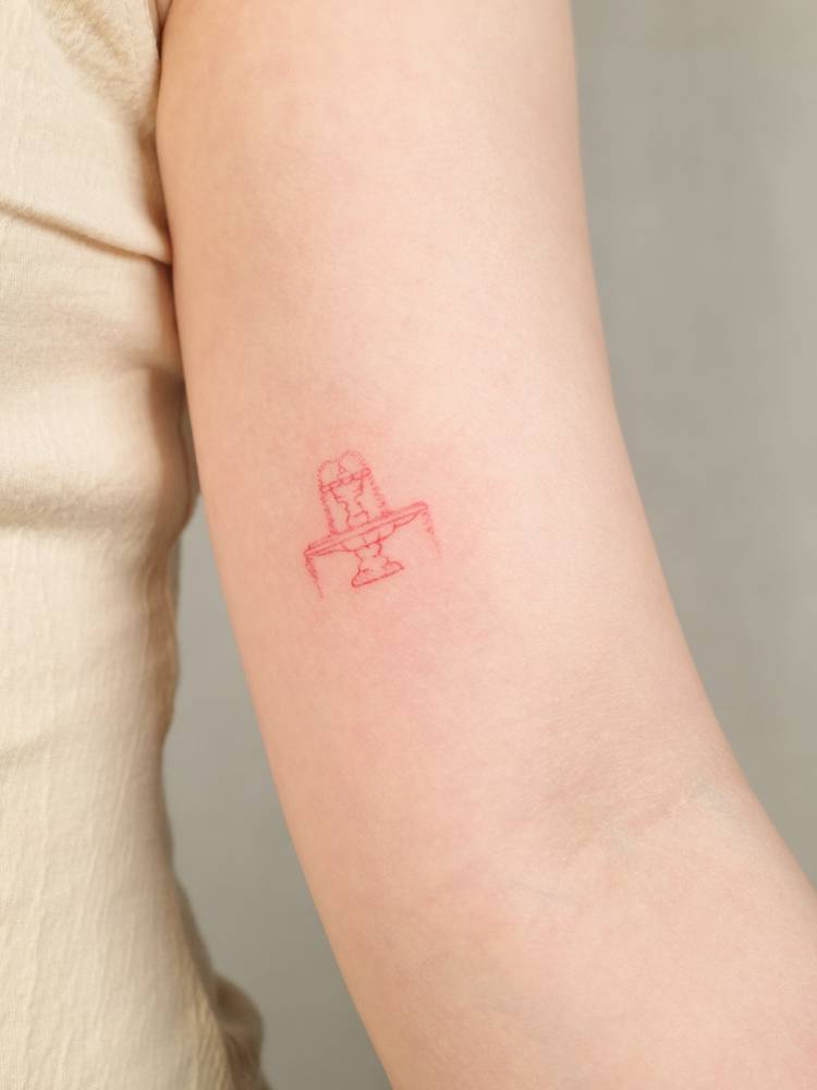 Red fountain tattoo located on the inner arm, fine line style.
