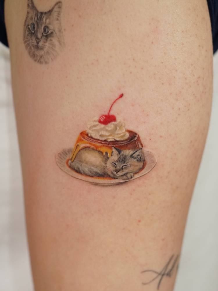 Cat pudding tattoo located on the upper arm, micro-realistic style.
