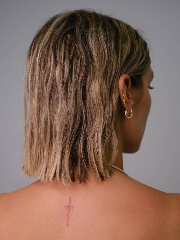 Little sword tattoo in fine line style located on the upper back.