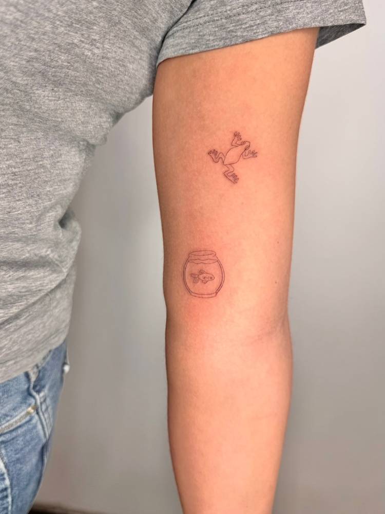 Fish bowl and frog tattoos located on the inner arm, done in fine line style.