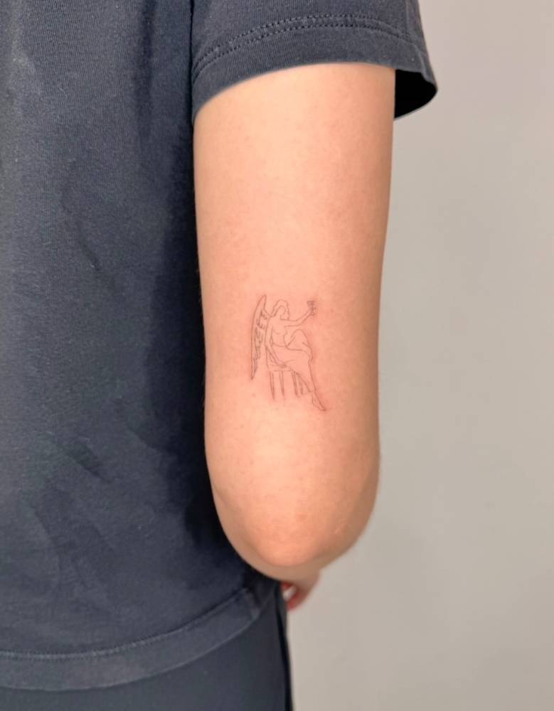 Little angel tattoo placed on the tricep, fine line style.