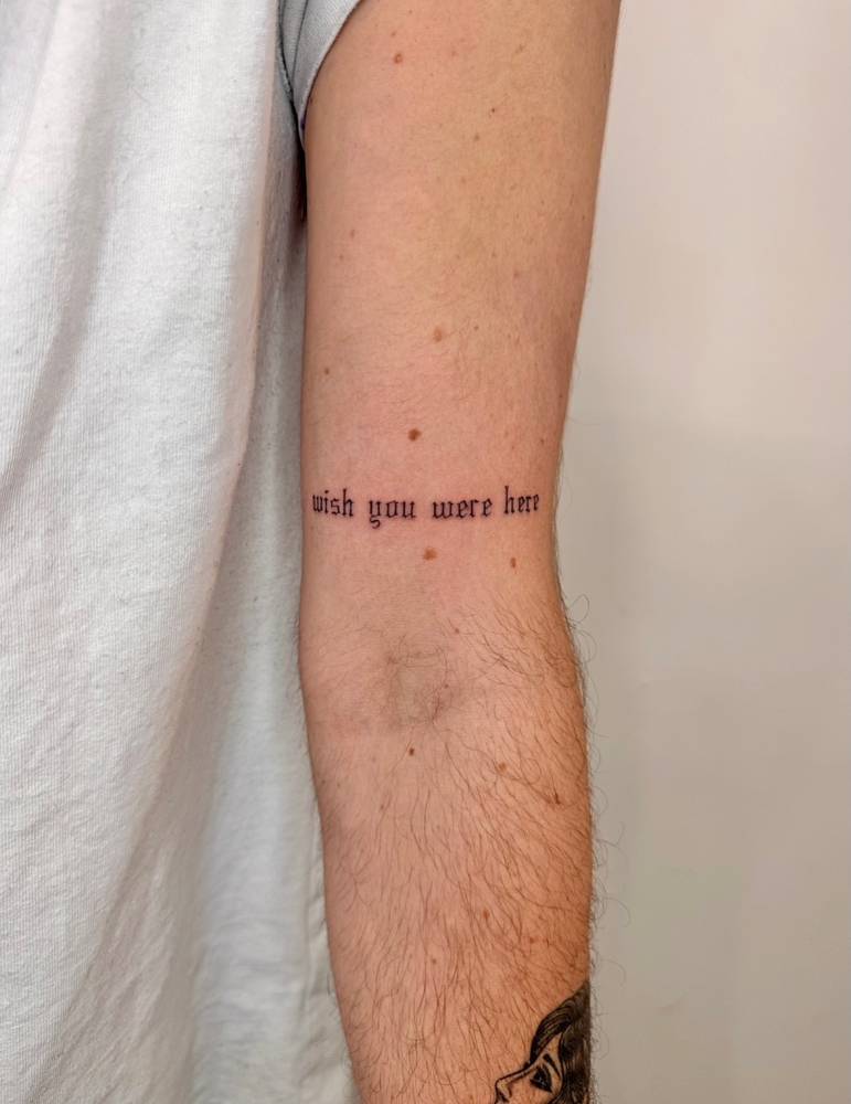 "Wish you were here" lettering tattoo in gothic font.