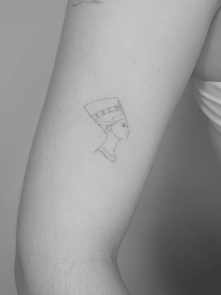 Fine line style Nefertiti tattoo located on the upper arm.