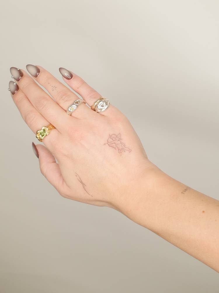 Tiny Cupid tattoo done in fine line style, located on the hand.