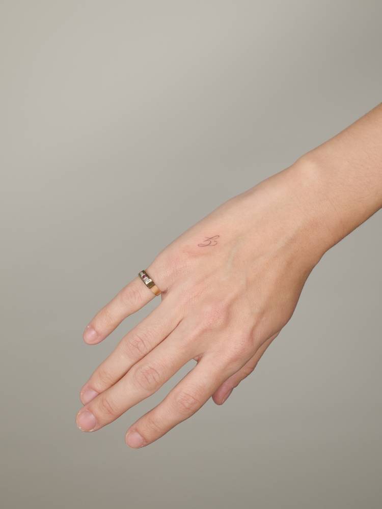 Script font letter "G" tattoo located on the hand.