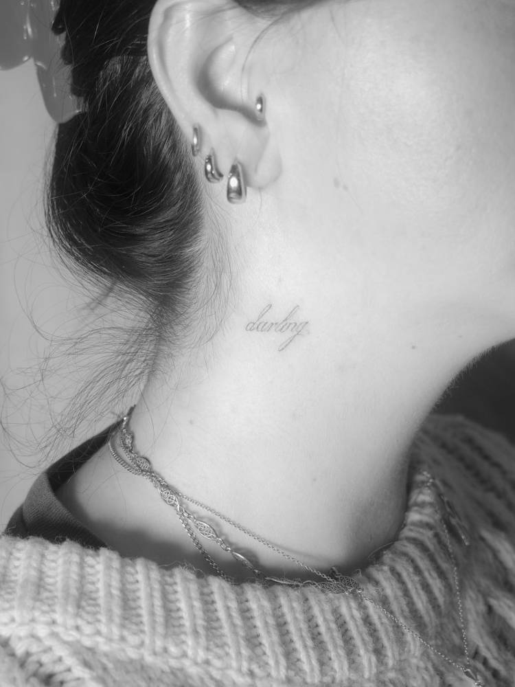 Lettering tattoo of the word "darling" in script font placed on the neck.