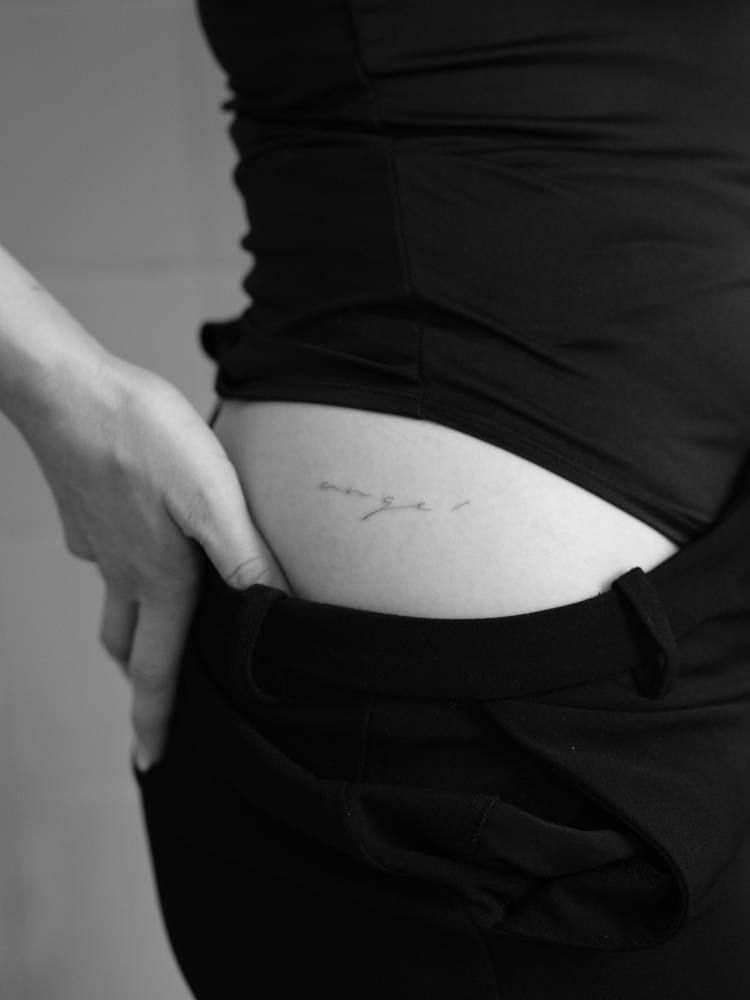 Handwritten font word "angel" tattooed on the hip.