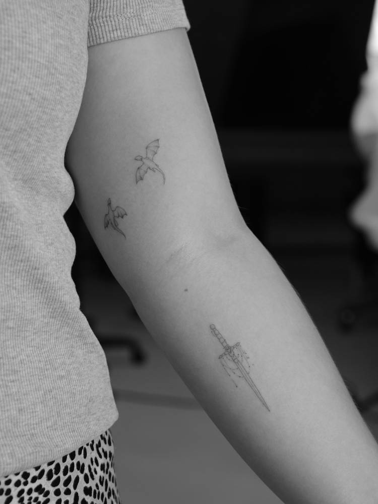 Dragons and sword tattoos in fine line style.