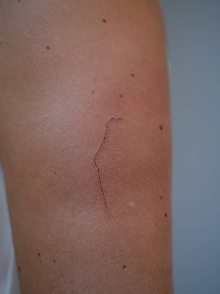 One line woman body tattooed on the upper arm, minimalistic style.