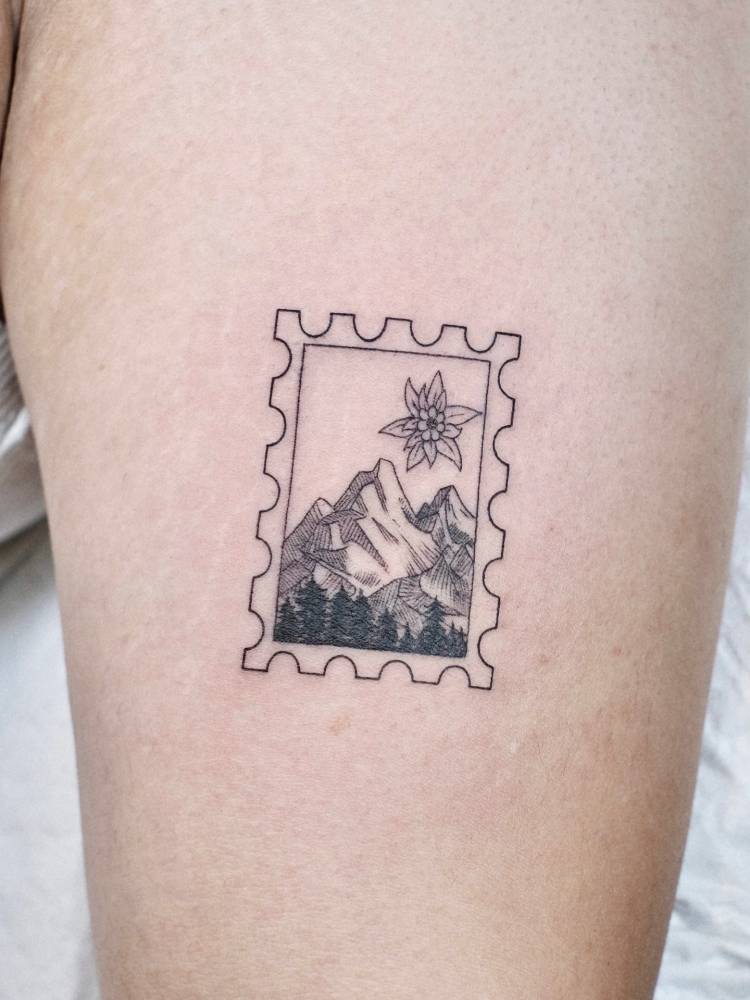 Edelweiss flower and mountain stamp tattoo located on the thigh.