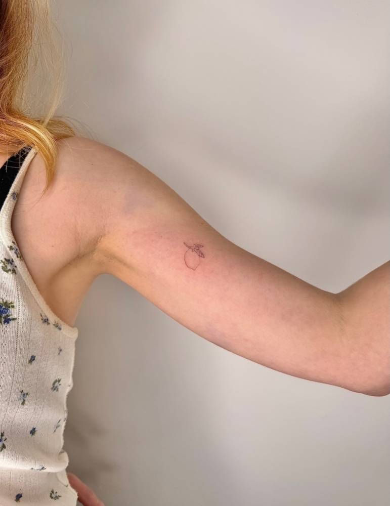 Minimalistic little lemon tattoo in fine line style located on the inner arm.