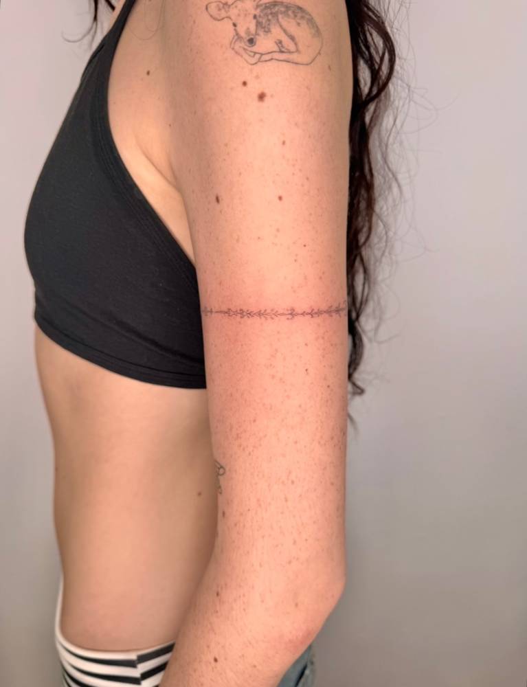 Ornamental bracelet tattoo located on the upper arm, fine line style.