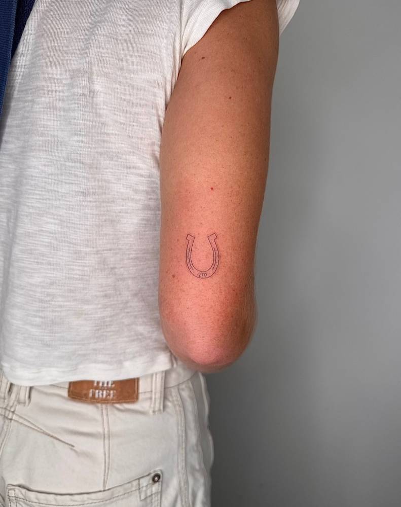 Lucky horseshoe tattoo located on the tricep, fine line style.