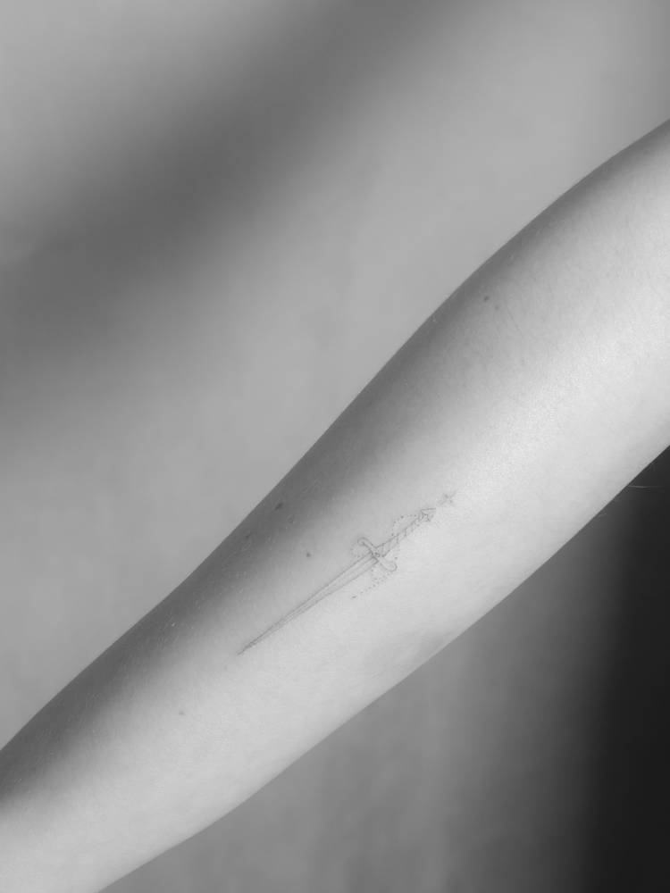 Sword in fine line style tattooed on the inner forearm.