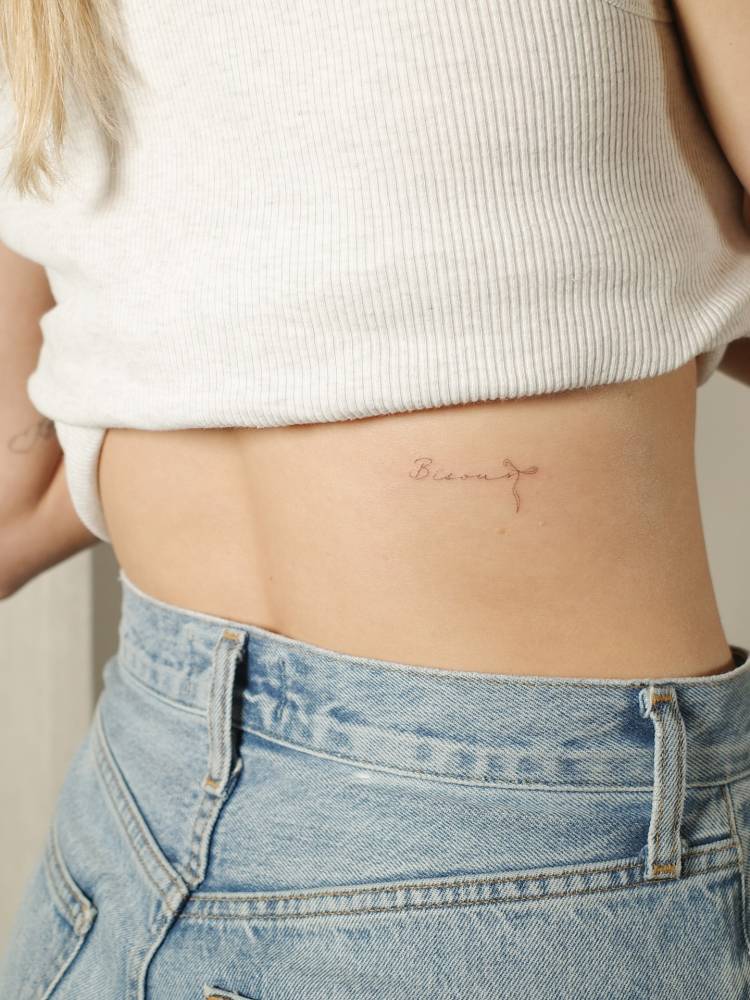 Handwritten font word "bisous" tattoo located on the lower back.