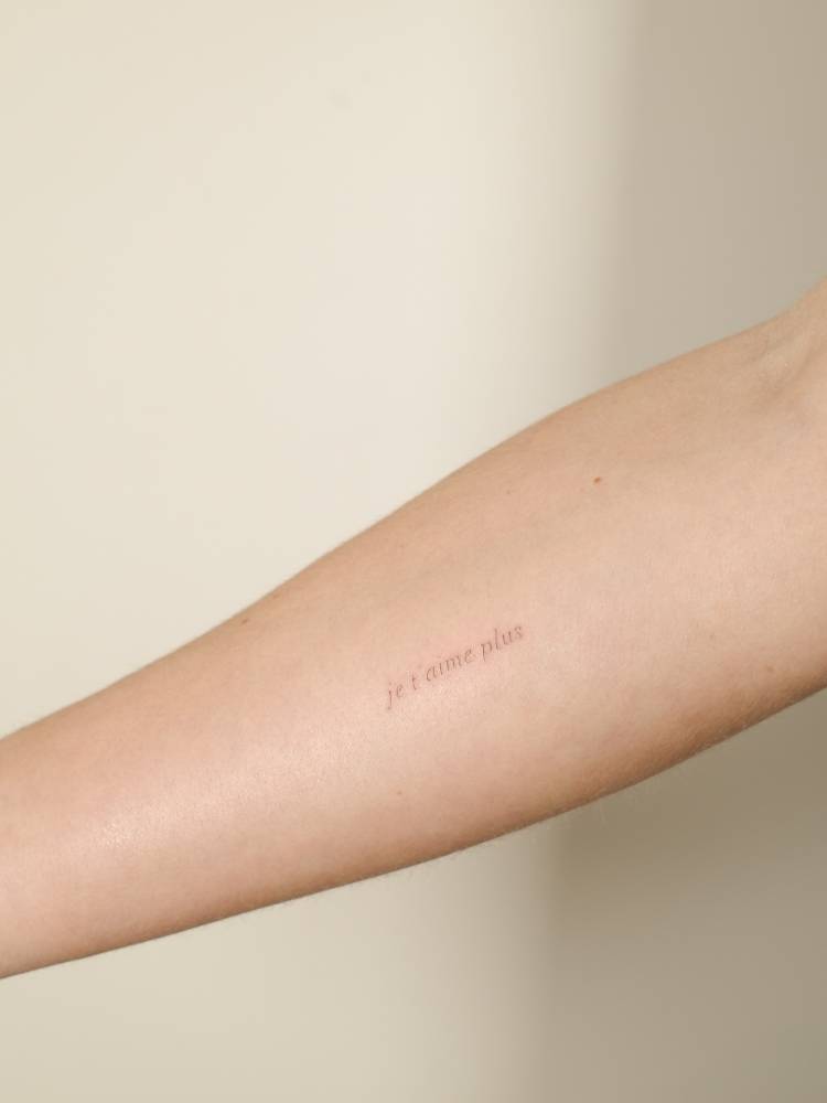 "Je t'aime plus" lettering tattoo located on the inner forearm.