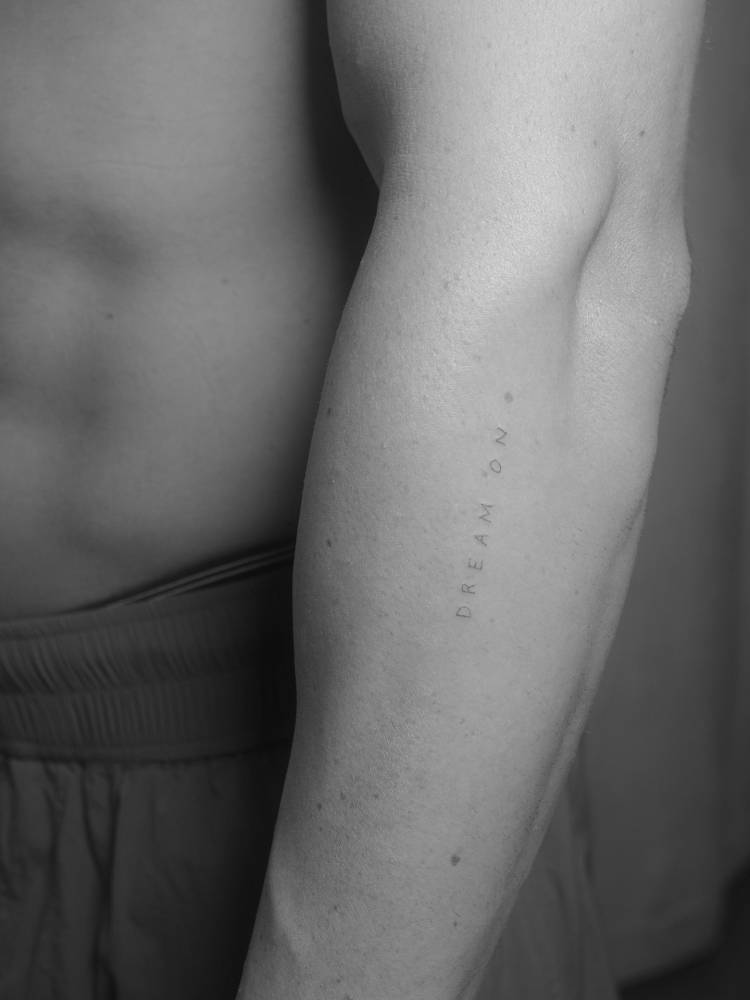 "Dream on" lettering tattoo in handwritten font done on the forearm.