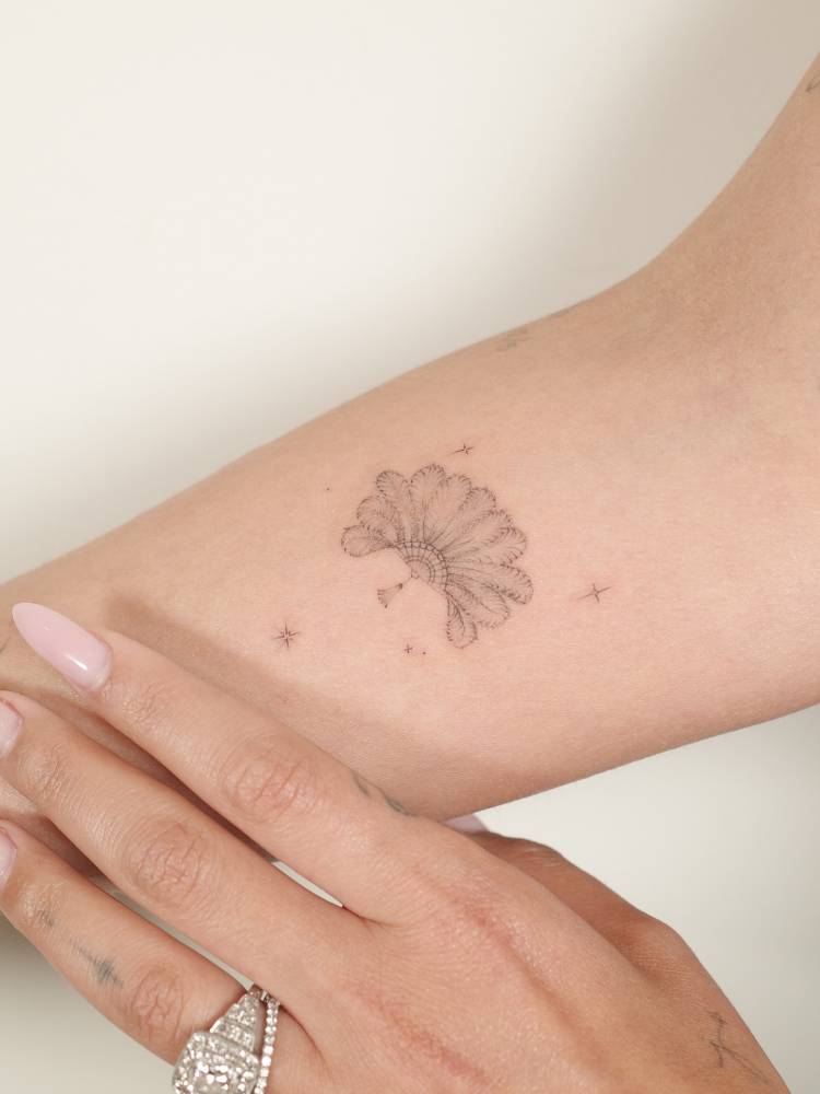 Feather hand fan tattooed on the inner forearm.
