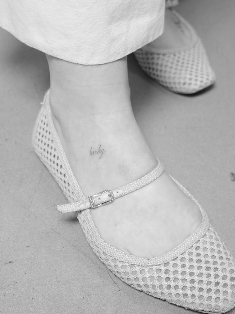 Script font word "lucky" tattoo placed on the foot.