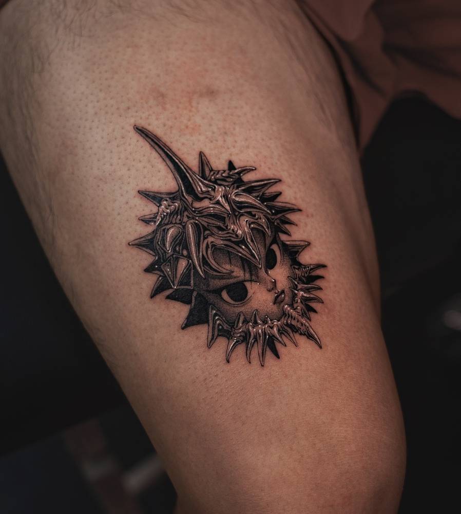 Cartoon style face and thorns tattoo located on the thigh.