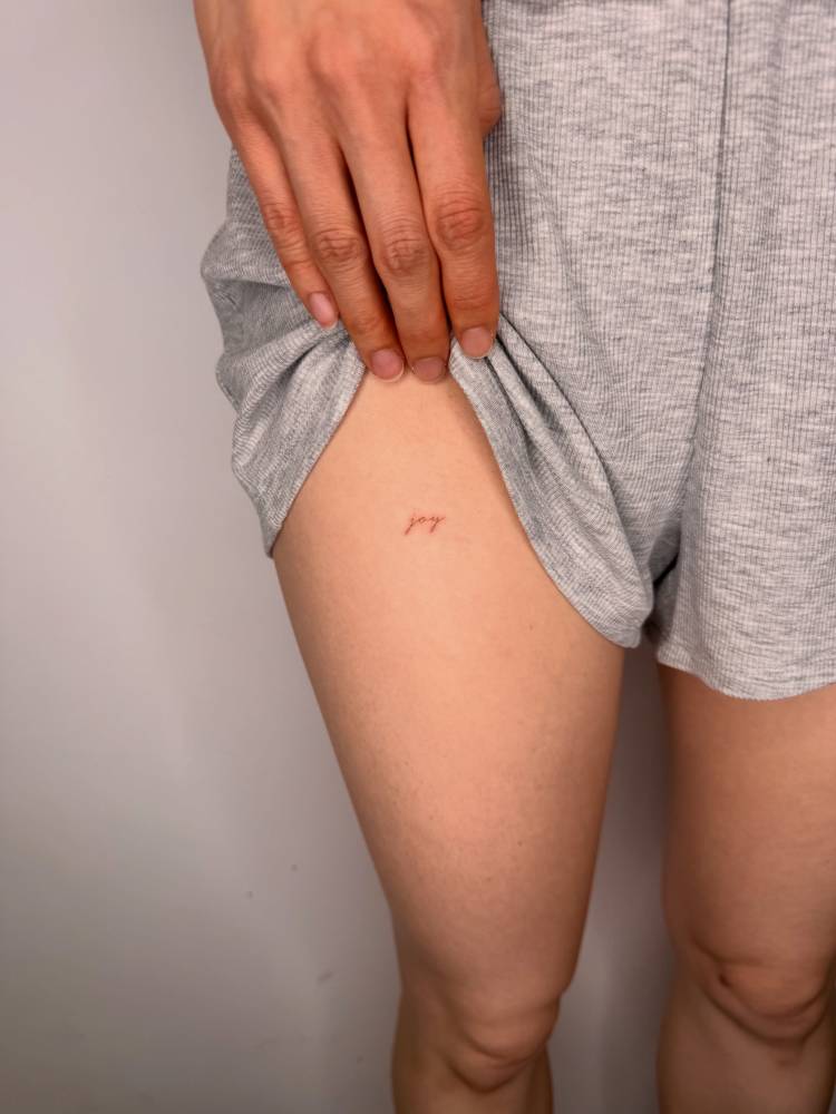 Handwritten font word "joy" tattoo placed on the thigh.
