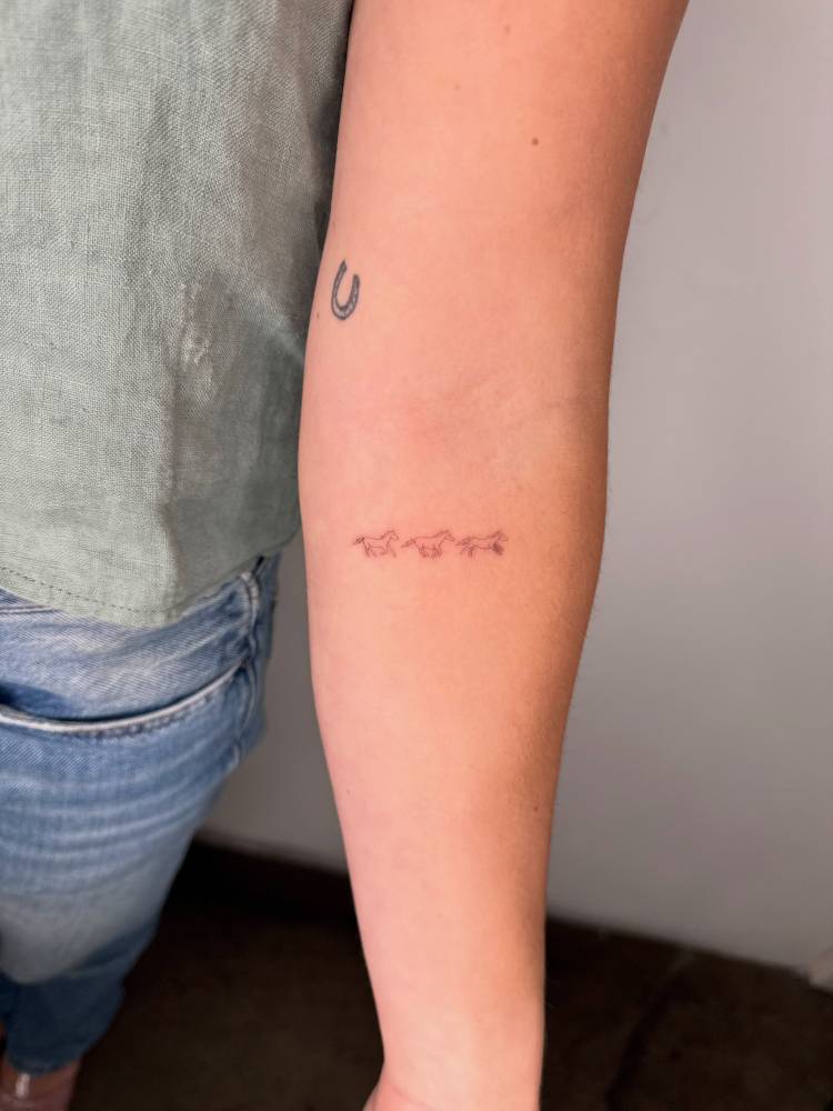 Tiny little horses in fine line style tattooed on the inner forearm.
