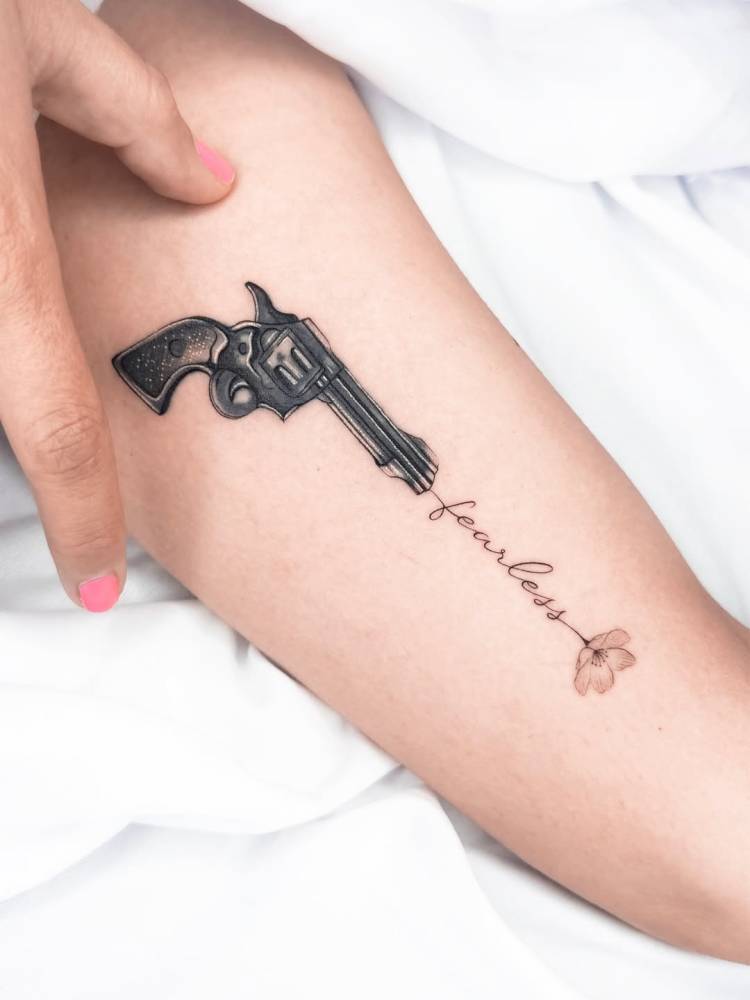 Revolver and word "fearless" tattooed on the inner arm.