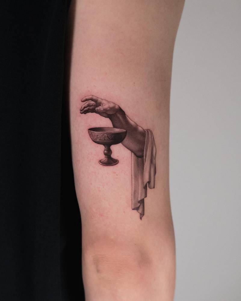 Micro-realistic style hand and chalice tattoo located on the tricep.