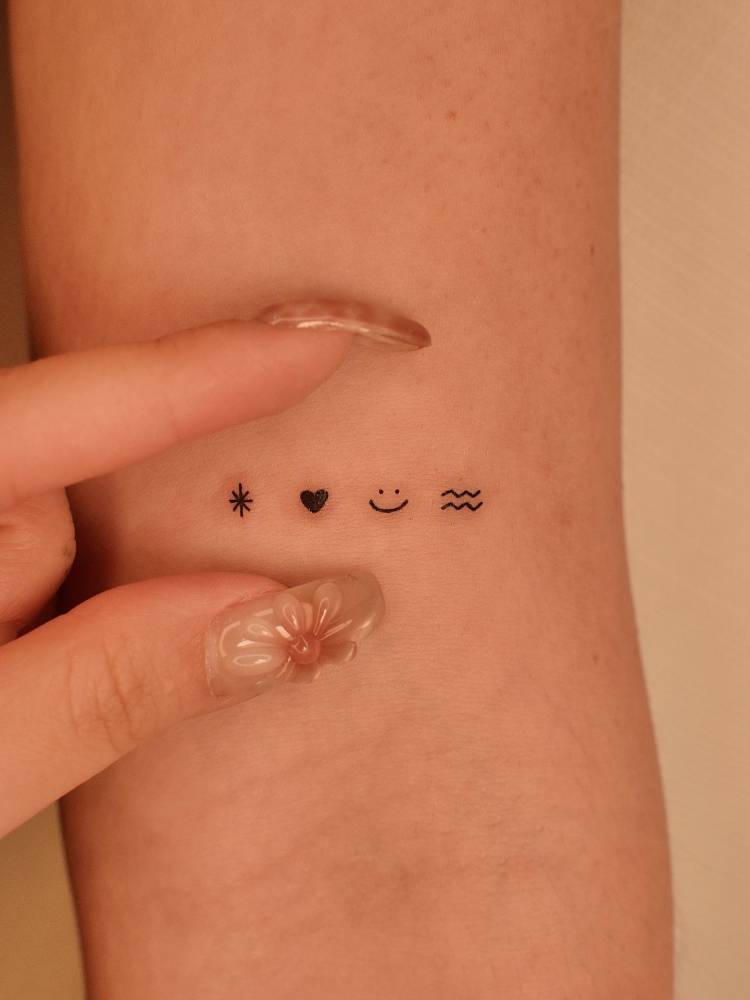 Star, heart, smiley face and Aquarius symbol tattooed on the bicep.