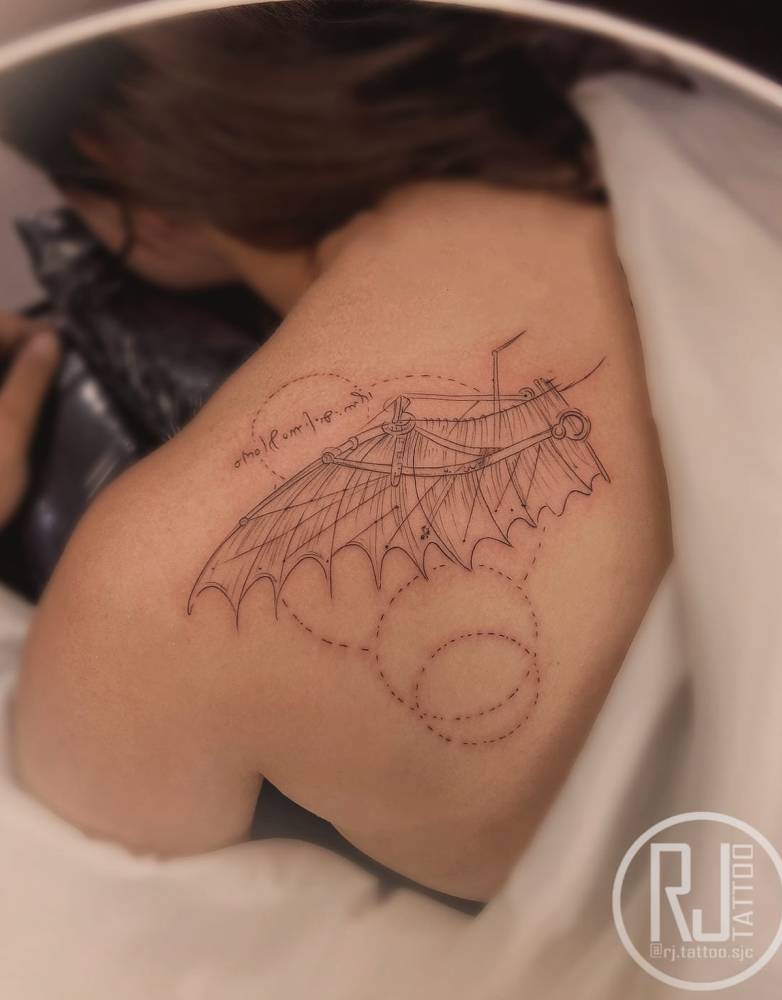 Da Vinci's wing tattoo on the shoulder blade, graphic style.