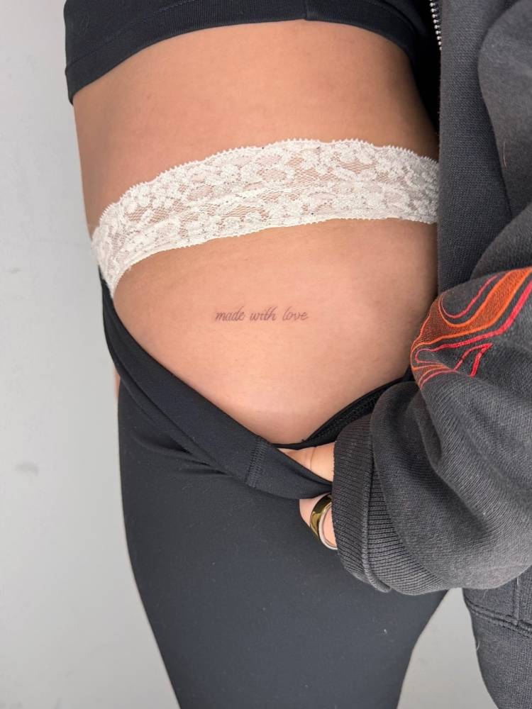 Lettering tattoo that says "made with love" located on the hip.