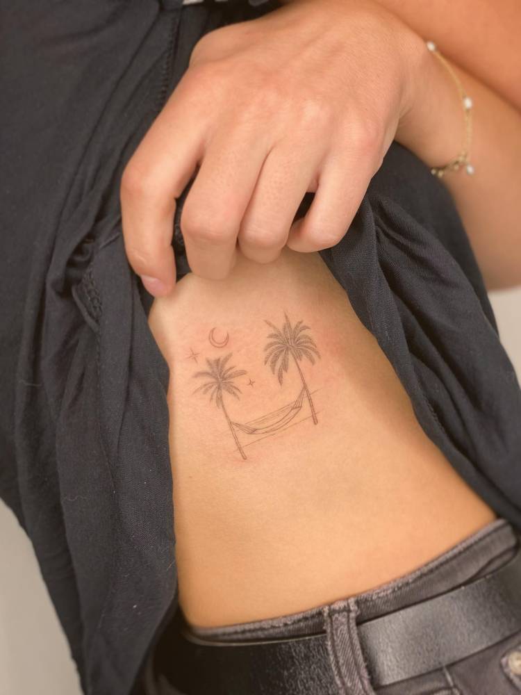Palm trees and hammock tattoo in fine line style located on the rib.