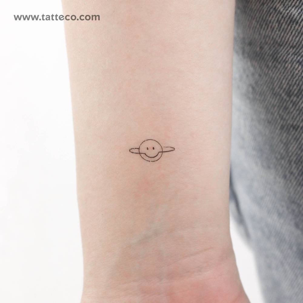 Minimalistic style smiley Saturn temporary tattoo located on the wrist.