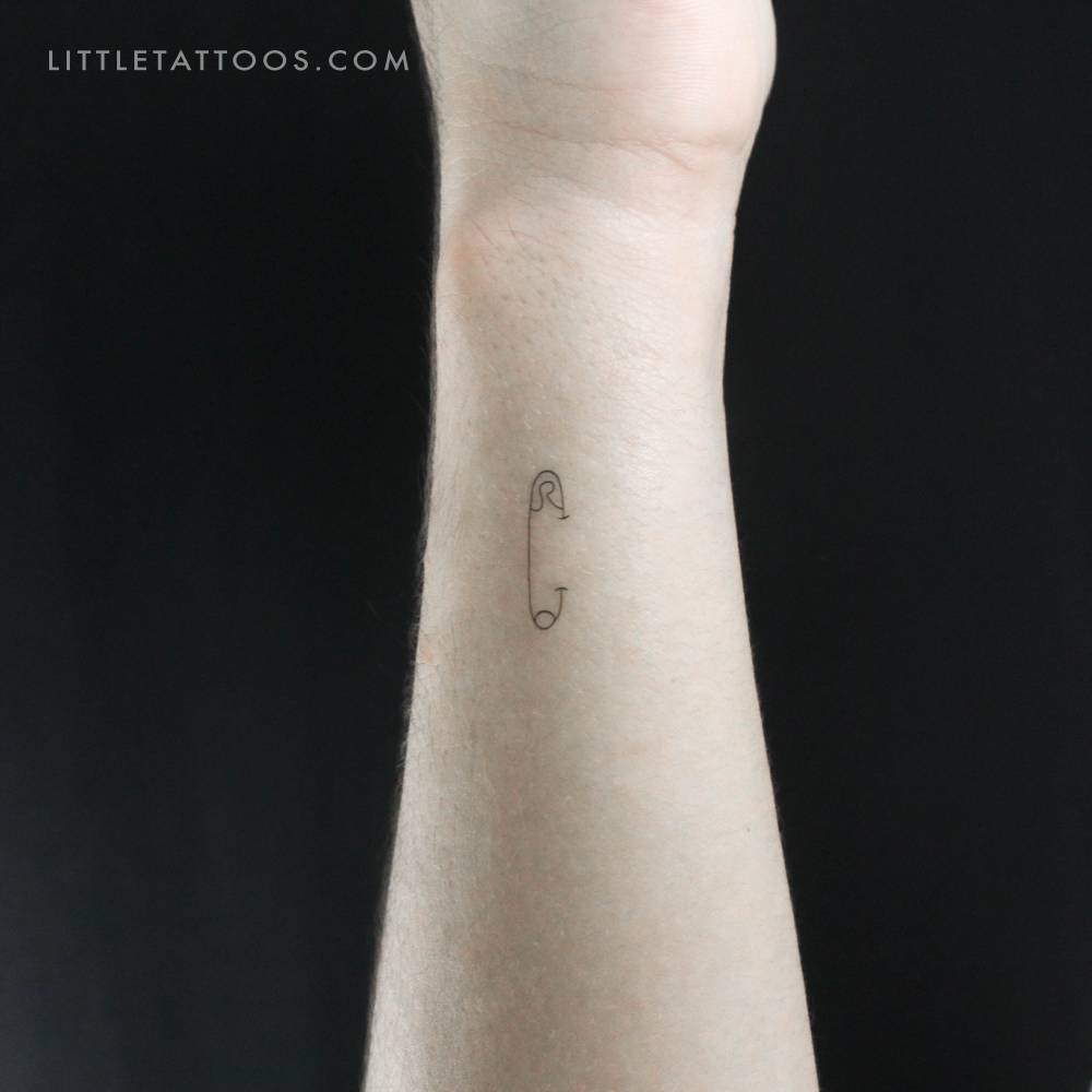Fine line style safety pin temporary tattoo located on the wrist.