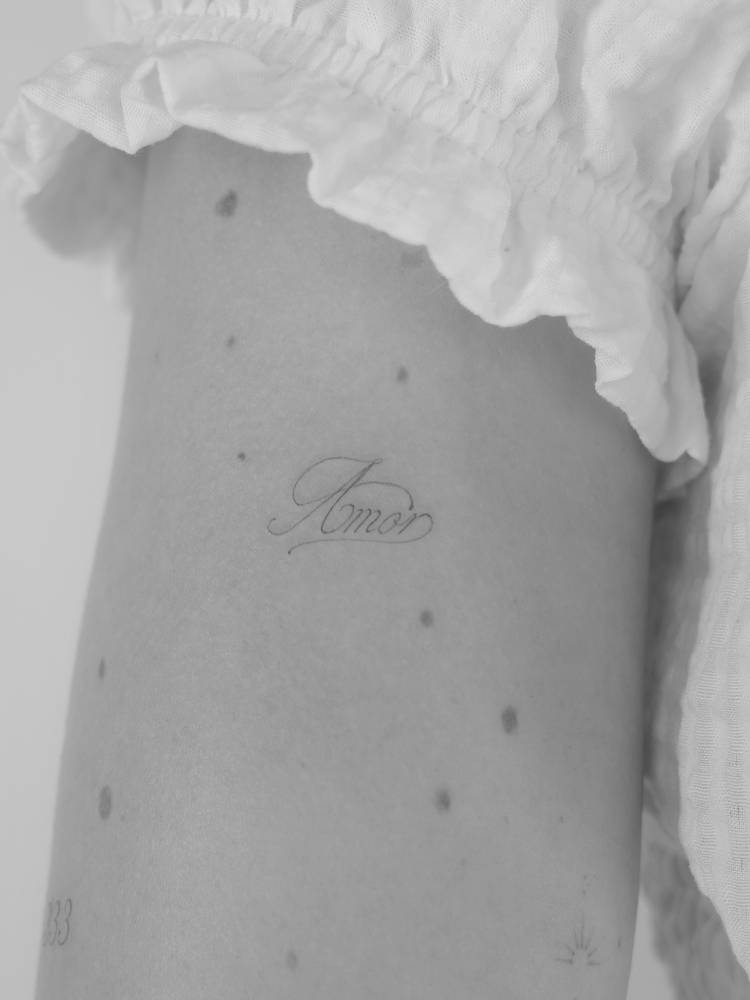 Script font word "amor" tattooed on the upper arm.