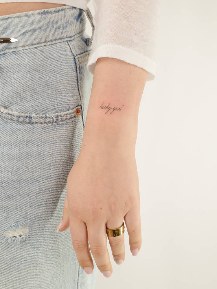 "Lucky girl" lettering tattoo in script font located on the wrist.