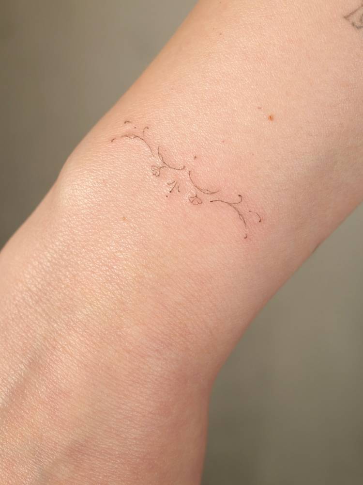 Tiny ornamental design tattooed on the wrist, fine line style.