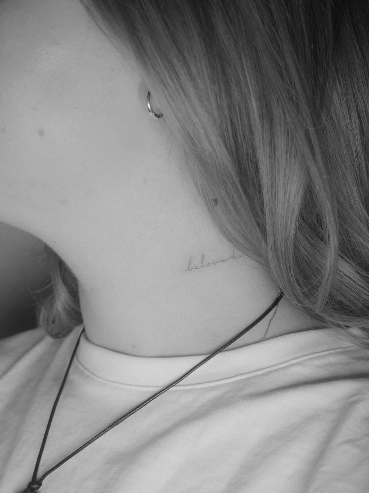 Handwritten font word "beloved" tattooed on the neck.