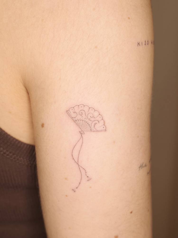 Hand fan in fine line style tattooed on the upper arm.
