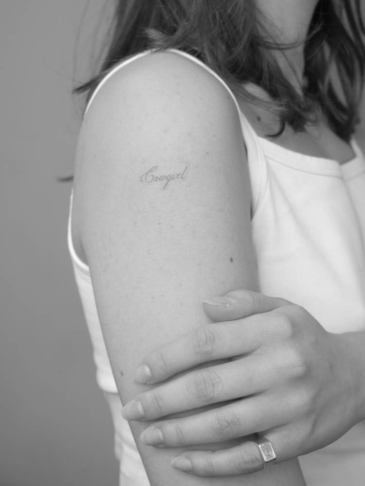 "Cowgirl" lettering tattoo located on the upper arm.