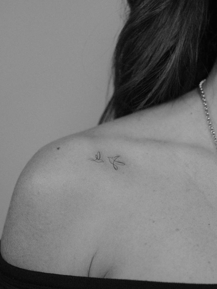 One line swallows tattooed on the shoulder, minimalistic style.