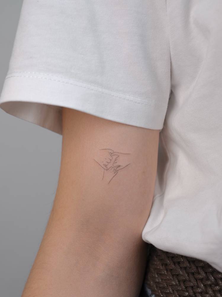 Fine line style pinky promise tattoo located on the bicep.